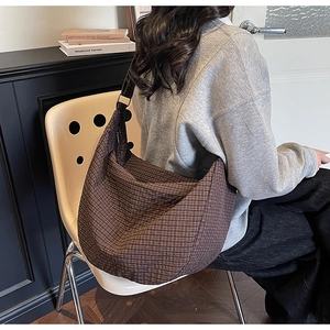 Bolso hobo a cuadros marrones con correa ancha llevado por una modelo en un entorno casual