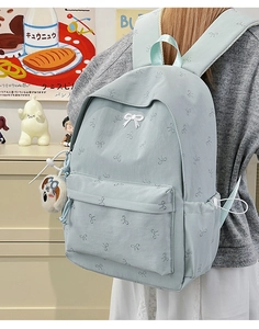 Detail view of light blue backpack with bow prints and cute dog charm on model in a room