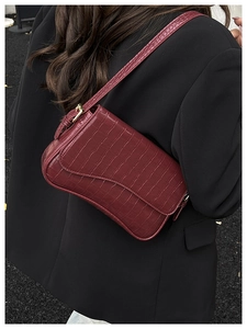 Detail shot of a dark burgundy crocodile textured handbag on a model in a black suit