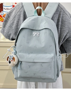 Detail of light blue backpack featuring bow print and a cute plush puppy pendant