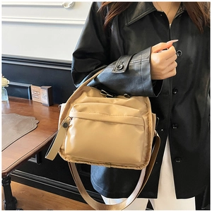 Detail of the front zipper pocket and wide shoulder strap on the khaki nylon crossbody bag