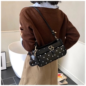 Detailaufnahme der schwarzen gepunkteten Achseltasche mit Herzanhänger auf der Schulter