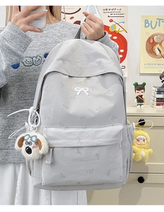 Detail view of light grey backpack with white bow prints and plush dog accessories