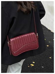Close-up of a burgundy croc-effect leather crossbody bag worn on a woman's shoulder