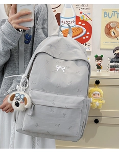 Detail of light grey backpack with bow pattern and plush charms in indoor setting