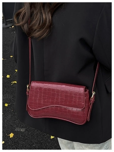 Detail of burgundy crocodile-embossed shoulder bag with gold hardware worn by a model