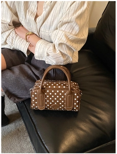 Close-up of brown polka dot boston bag with BROBOOM logo on a leather sofa