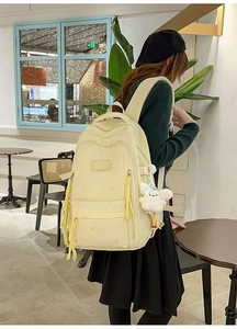 Detail view of a light yellow nylon backpack featuring multiple pockets and a plush pendant
