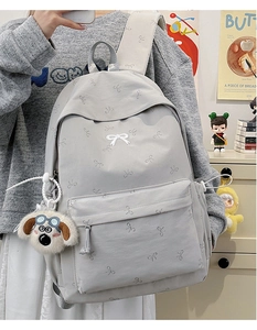 Detail of light gray backpack with bow pattern and plush puppy pendant accessory