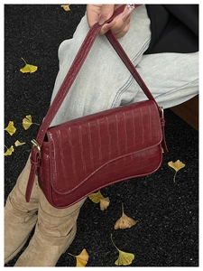 Close-up of burgundy crocodile pattern leather bag with gold buckle on autumn leaves