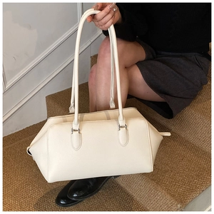 Borsa bowling in pelle color crema con trama litchi portata a spalla da una modella