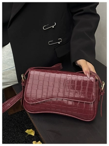 Detail of burgundy crocodile pattern leather shoulder bag with magnetic flap and gold hardware