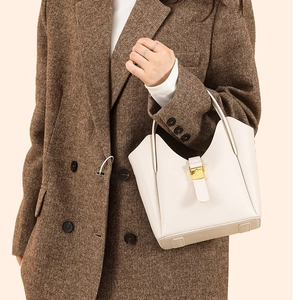 Sac seau chic en cuir grainé beige avec boucle dorée, porté par un mannequin élégant