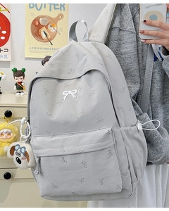 Detail view of light grey canvas backpack featuring white bow patterns and plush dog charm