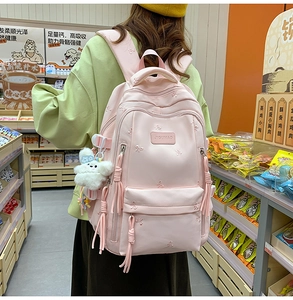Close-up of pink school backpack featuring bow embroidery and a fluffy white plush toy