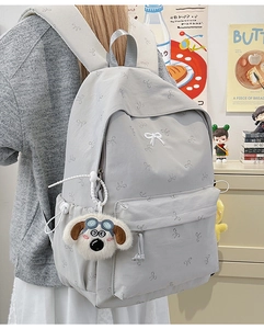 Detail of light gray backpack with bow pattern and cute puppy plush pendant in study room