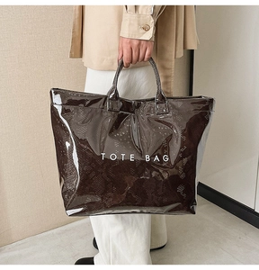 Detail of glossy snake pattern tote bag featuring white TOTE BAG text and patent finish