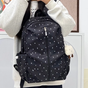Detail of black backpack with star patterns and cloud charm worn by a model