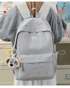 Close-up of light gray canvas backpack with bow patterns and plush dog charm detail