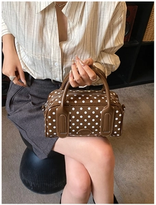 Close-up of a brown polka dot Boston bag with leather handles and brand logo tag