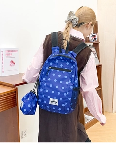 Detail of navy blue polka dot backpack and matching pouch in a cozy library setting