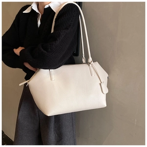 Detail of minimalist cream calfskin leather tote bag worn by a model in a studio setting