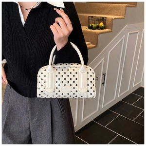 Close-up of white polka dot Boston handbag featuring glossy finish and brand plaque detail