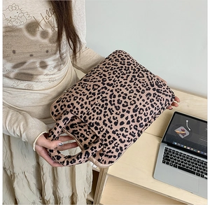 Detail of soft leopard print laptop sleeve with handles being held near a wooden desk