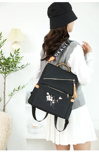 Détail d'un sac à dos en nylon noir avec broderie florale et bandoulière texte BEAUTY