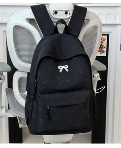 Detail view of black backpack with bow print and 3D white bow hanging on a chair