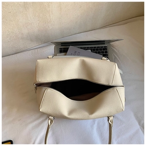 Top view of beige lychee leather tote bag interior with laptop on white bedding