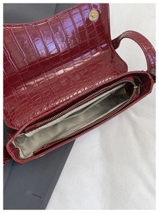 Detail of burgundy crocodile pattern handbag with magnetic closure and zippered inner pocket