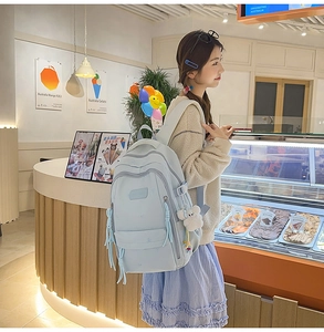 Light blue multi-pocket backpack with cute bear pendant shown on model in a cafe