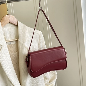 Detail view of burgundy leather shoulder bag with gold hardware on a minimalist hanger