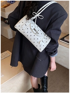 Close-up of white shoulder bag with black polka dots and decorative bow on the strap