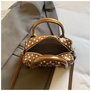 Brown polka dot handbag with dual handles and crossbody strap on a blazer background