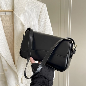 Detail of matte black baguette bag with gold metal buckle and leather shoulder strap