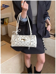 Detail of white polka dot shoulder bag with bow decoration and metal heart pendant