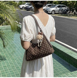 Close-up of brown polka dot dumpling bag with a plush sheep charm in an outdoor setting