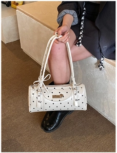Detail showing white polka dot handbag with bow accents and metal logo plaque