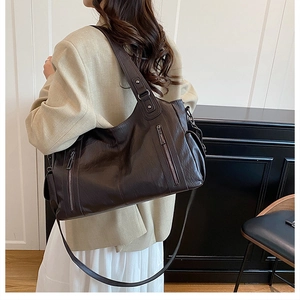 Detail view of brown large capacity tote bag with glossy leather texture and metal zippers