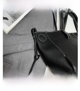 Detailed view of black lychee leather tote with white contrast stitching and magazine