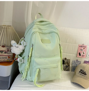 Close-up of mint green nylon backpack with bow embroidery and rabbit plush charm