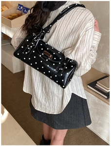 Detailed shot of black polka dot cylinder shoulder bag with silver metal lock closure