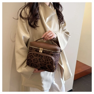 Detail of leopard print cosmetic bag with gold zippers and brown leather handle