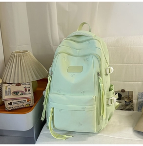 Detail of light green backpack showing white bow embroidery and multiple zipper pockets