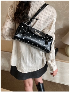 Close-up of black polka dot shoulder bag with silver buckle and shiny faux leather texture