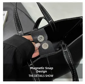 Detail of magnetic snap closure on black leather tote bag with white contrast stitching