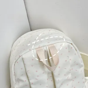 Detail of reinforced canvas handle and pink star pattern on the beige backpack