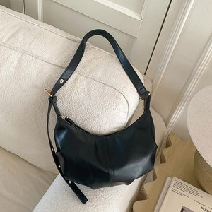 Premium black hobo shoulder bag with pleated leather texture on a cream sofa